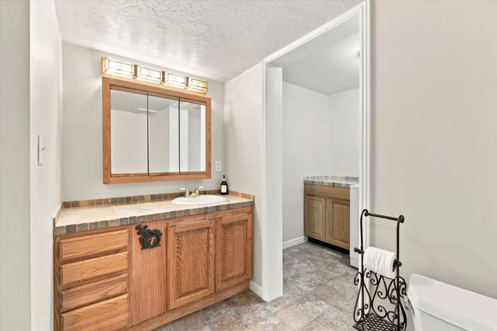 Bathroom featuring a wood vanity with a drop-in sink, a tiled countertop, and a medicine cabinet with integrated lighting
