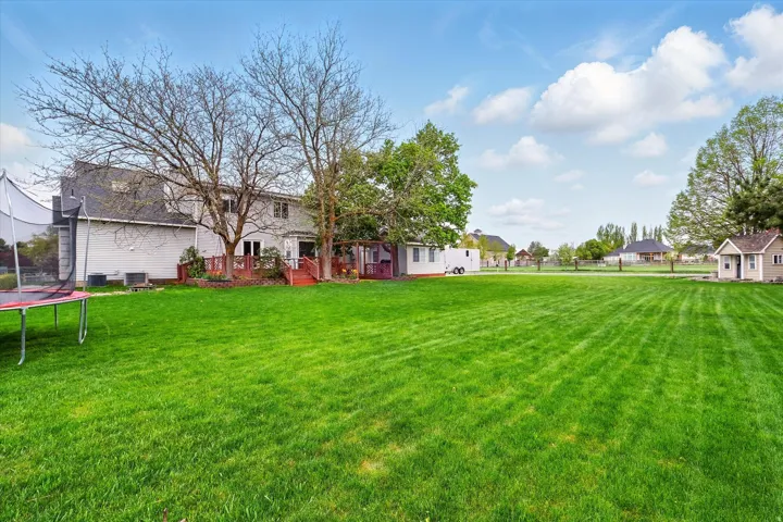 Expansive grassy yard featuring a multi-level wood deck, mature trees, and a detached shed