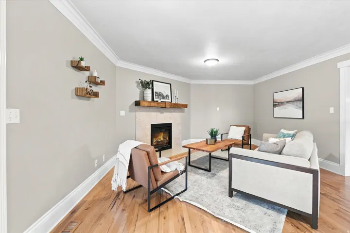 Living area featuring a stone-surround fireplace with a wood mantel, crown molding, light wood-finish flooring, and light neutral wall paint