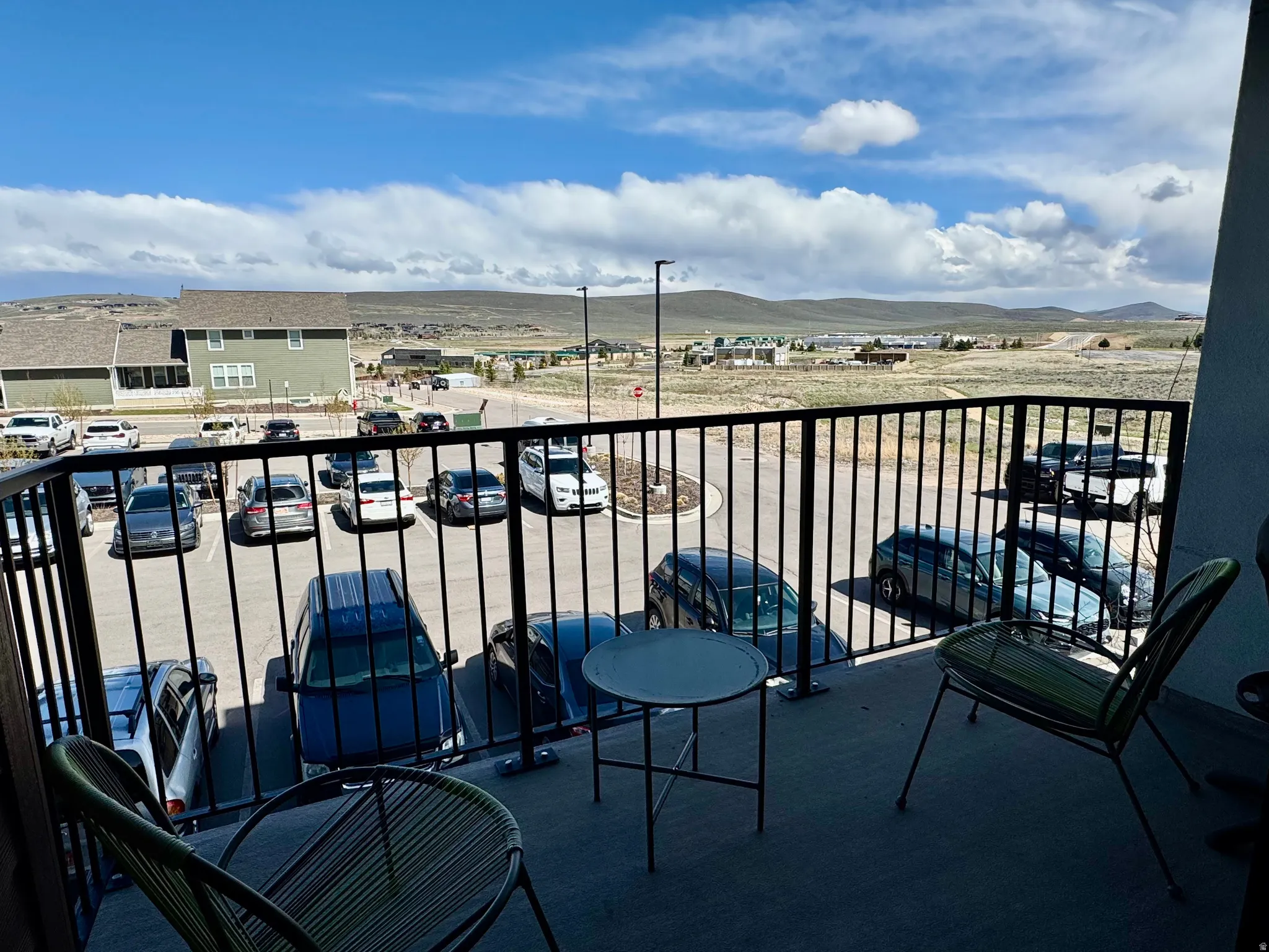 Concrete balcony with black metal railings overlooking a parking area and expansive distant landscape