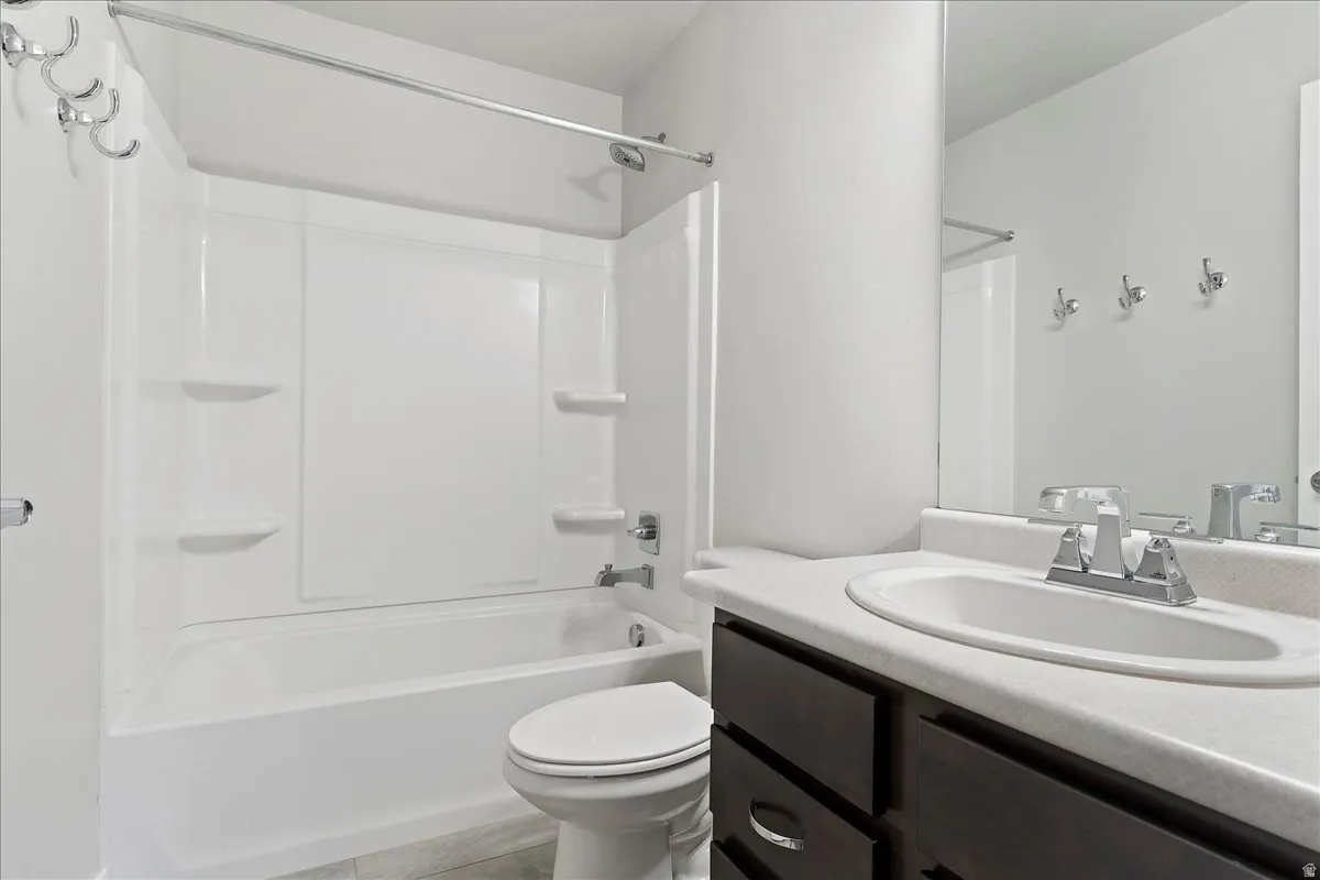 Full bathroom featuring a white tub and shower combination with built-in shelving, dark wood-finish vanity with an integrated sink, chrome fixtures, and a large wall-mounted mirror