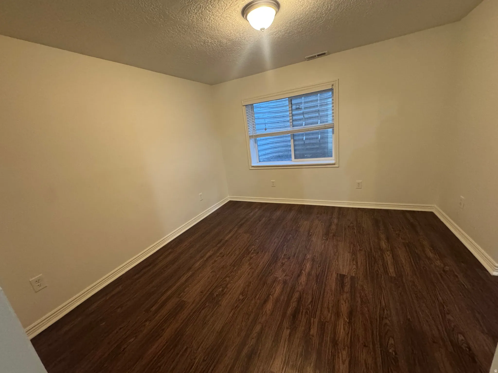 Room featuring wood-finish flooring, neutral wall paint, white trim, a single window with blinds, and an overhead flush-mount light fixture