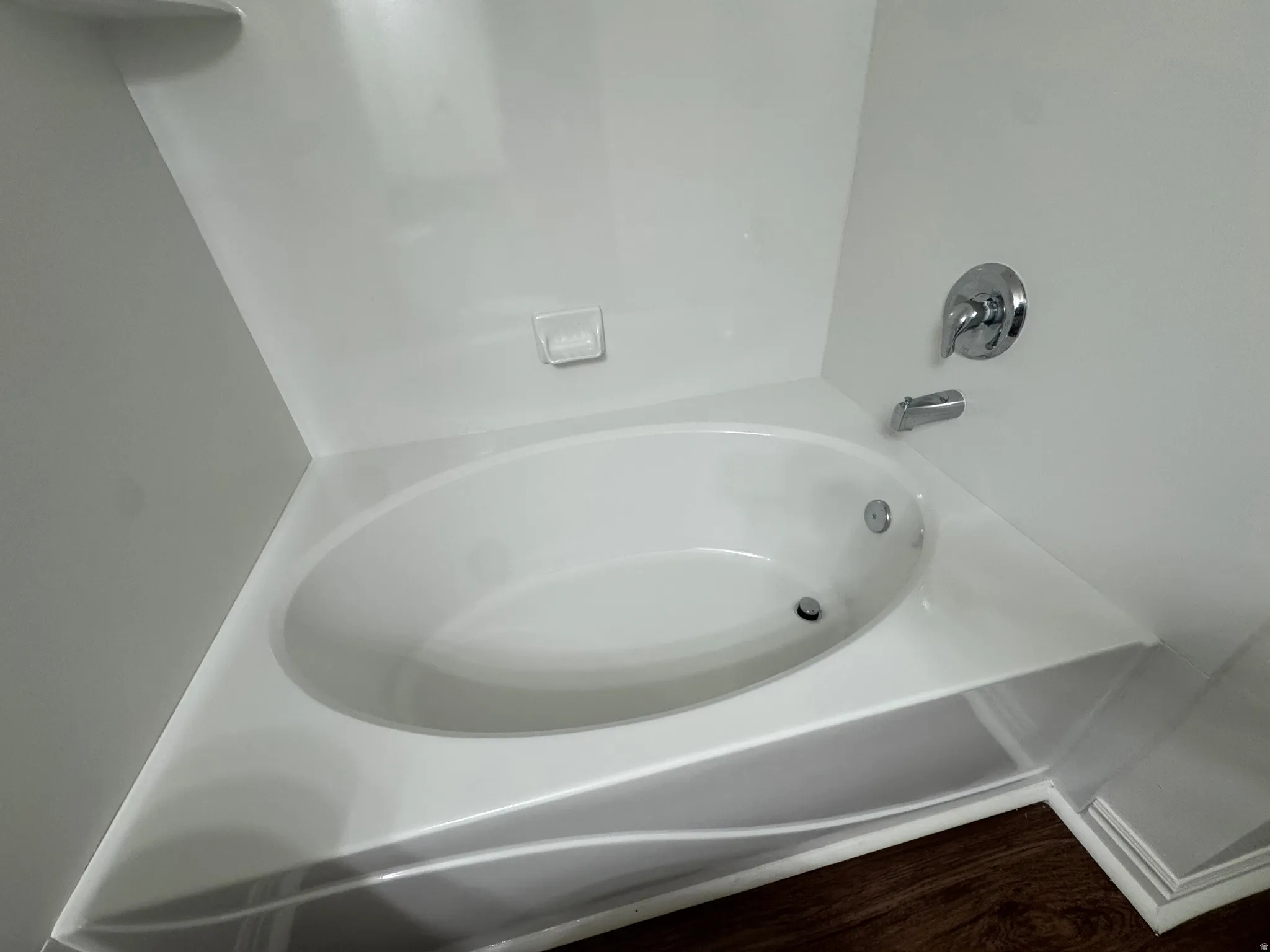 Built-in soaking tub with white surround, chrome fixtures, and dark wood-finish flooring