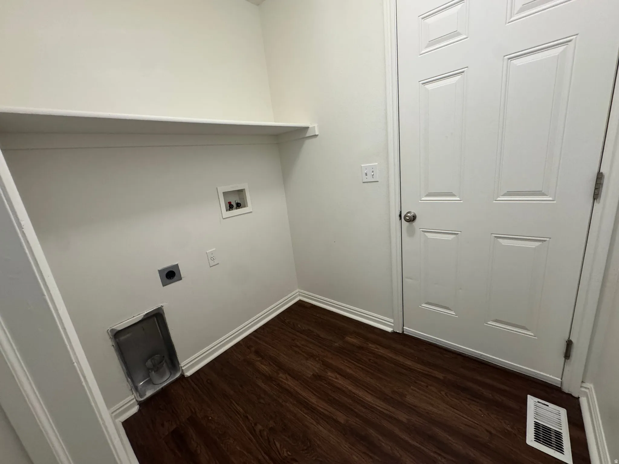 Dedicated laundry area featuring a white storage shelf, white paneled door, and dark wood-finish flooring