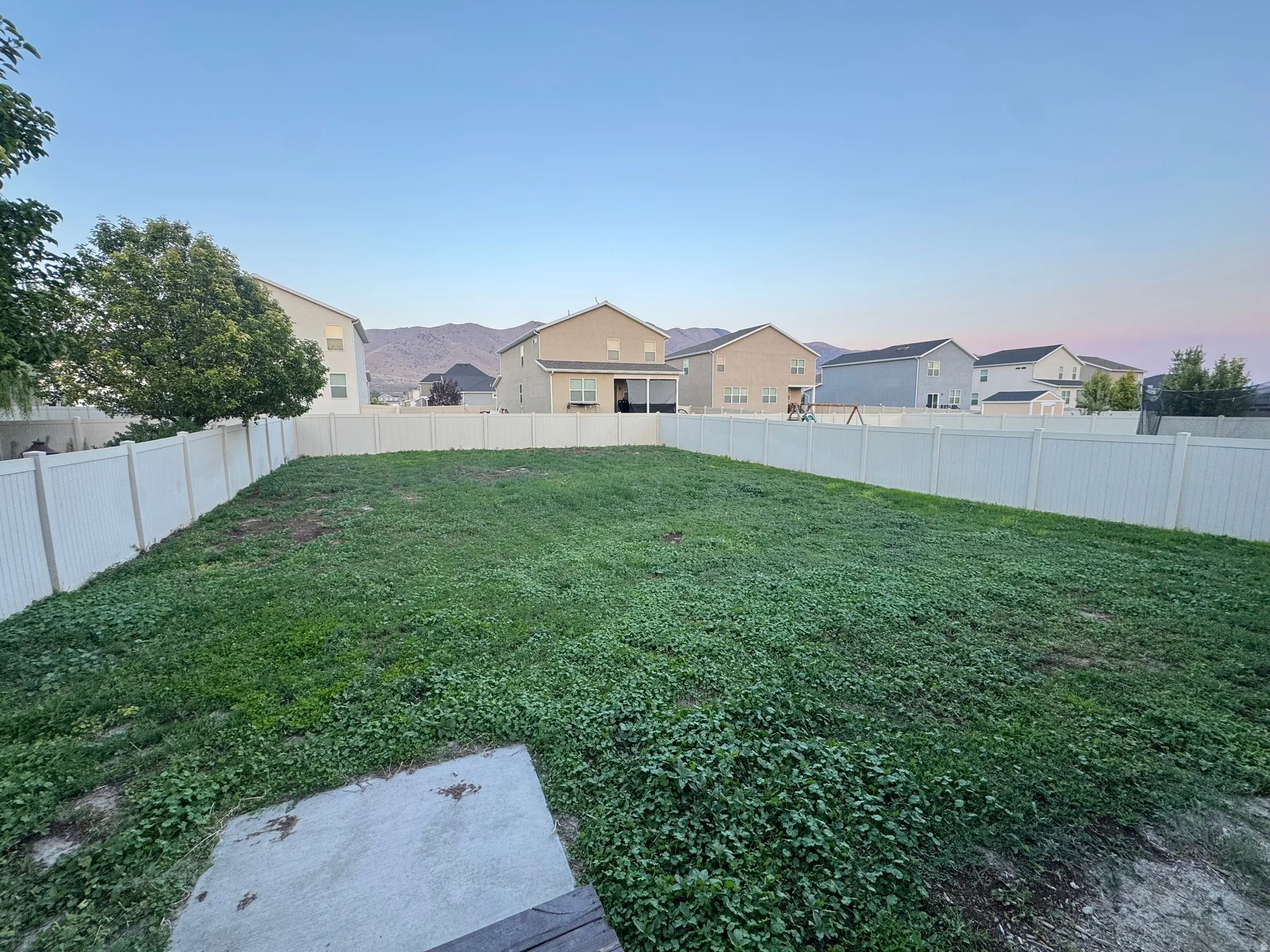 Expansive backyard featuring a large grassy area, privacy fencing, a concrete pad, and distant mountain scenery