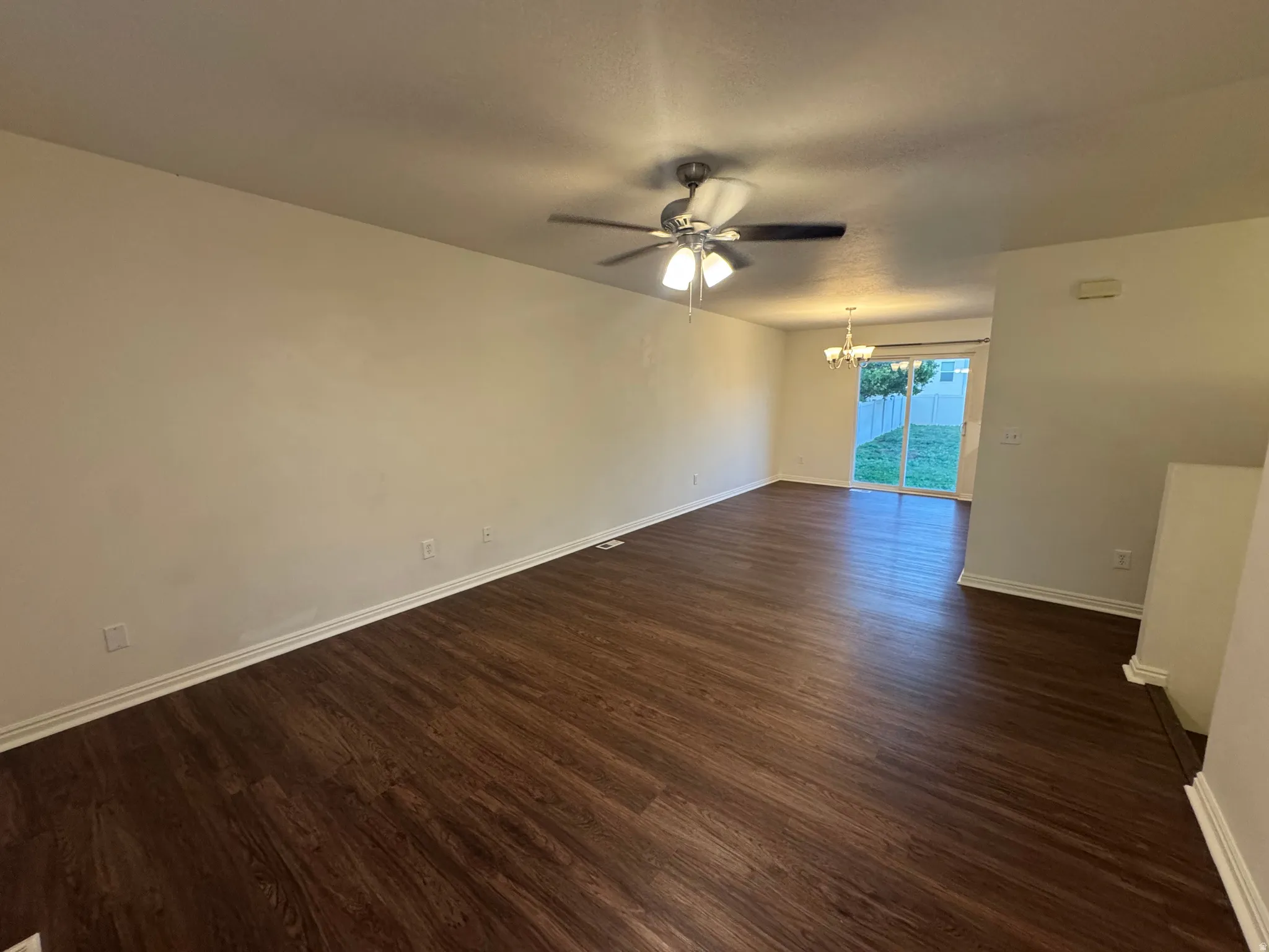 Spacious living area featuring wood-finish flooring, a ceiling fan with integrated lighting, and neutral wall tones