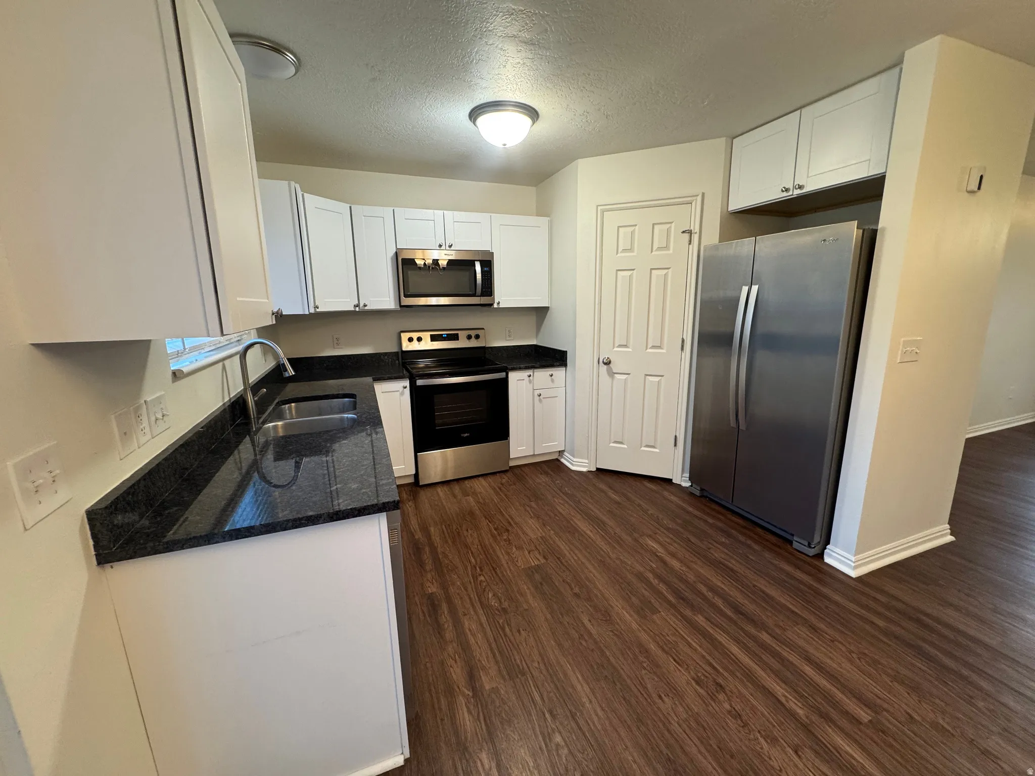 Kitchen featuring white cabinetry, dark stone countertops, stainless steel appliances, wood-finish flooring, and a recessed ceiling light fixture