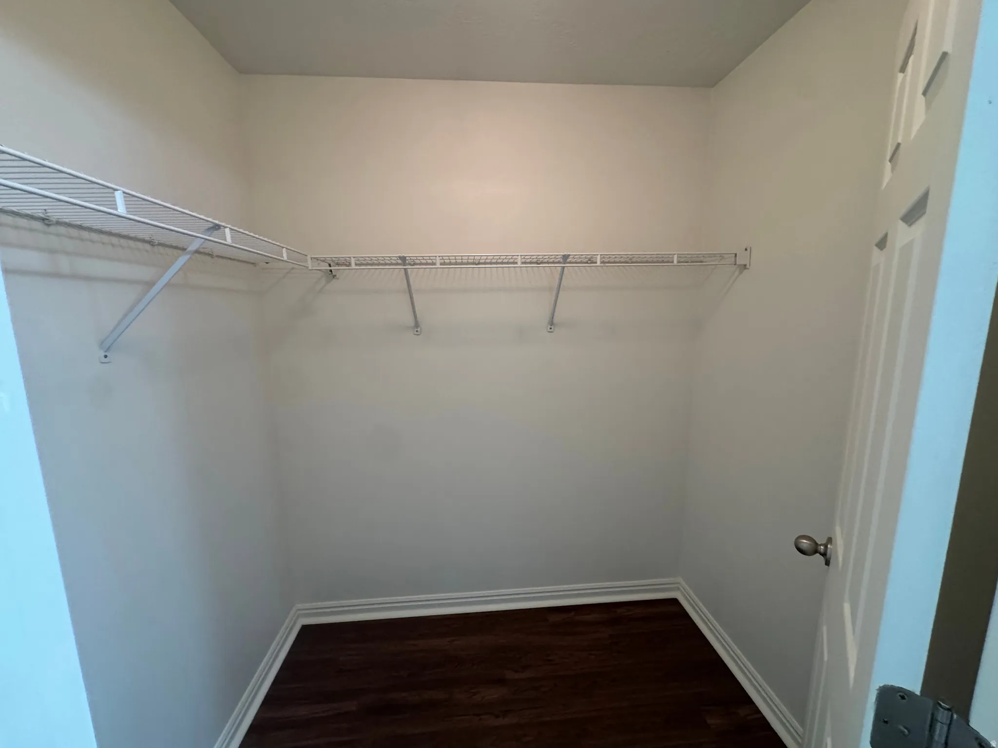 Walk-in closet featuring white wire shelving, white baseboards, and wood-finish flooring