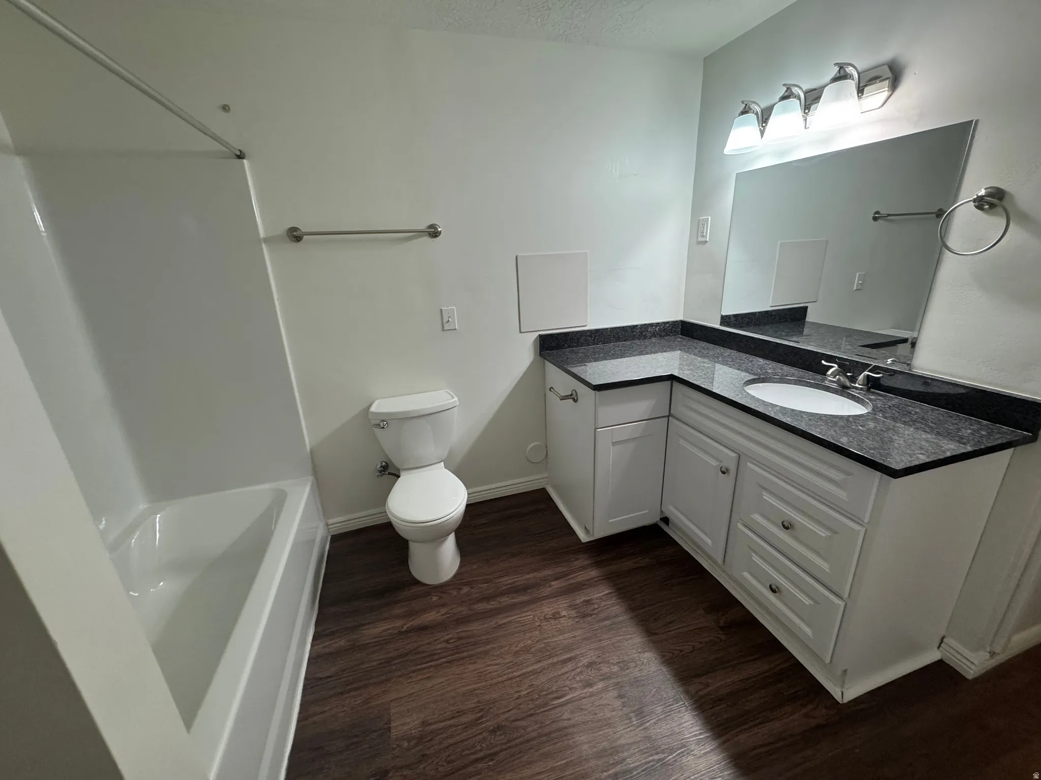 Bathroom featuring a white bathtub with shower, dark wood-finish flooring, and a white toilet