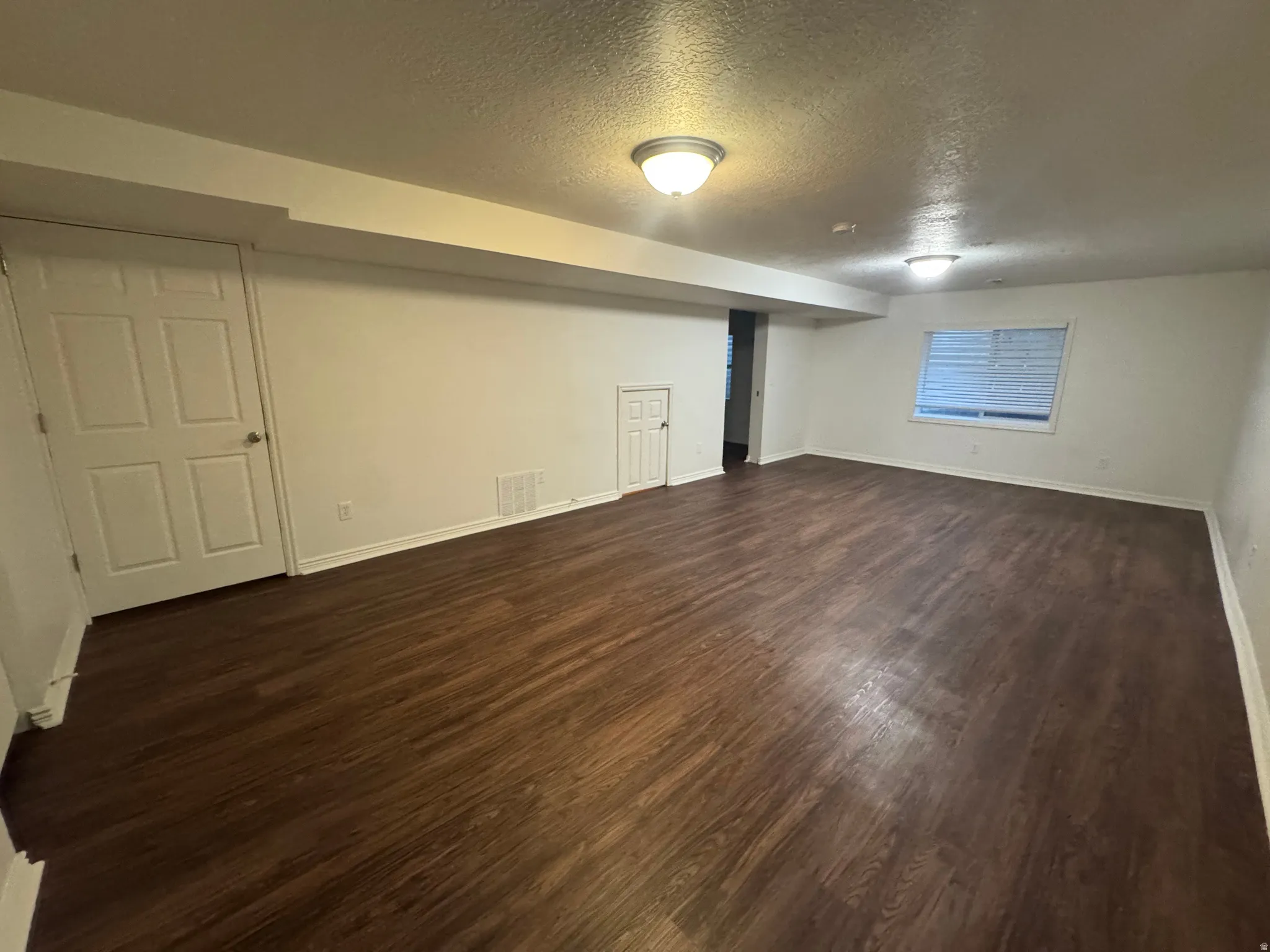 Spacious room featuring wood-finish flooring, white walls, and a visible window