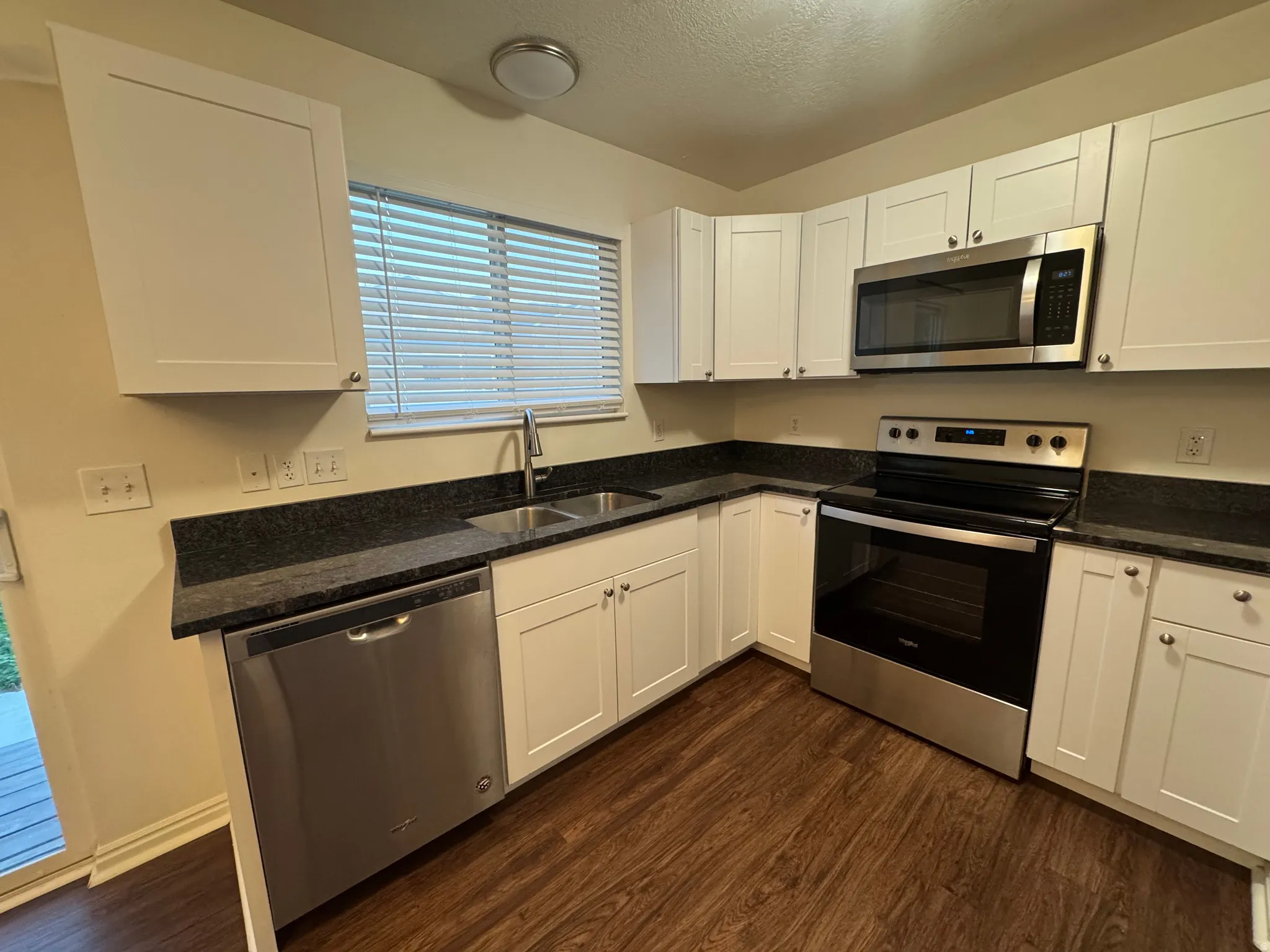 Kitchen featuring white shaker cabinetry, dark countertops, stainless steel appliances, and wood-finish flooring