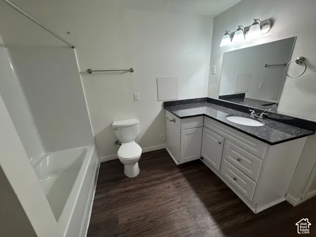 Bathroom featuring a white bathtub with shower, dark wood-finish flooring, and a white toilet