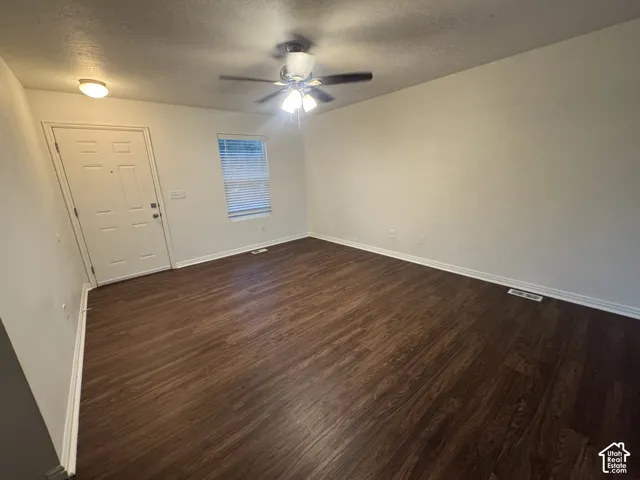 Spacious room featuring rich wood-finish flooring, a ceiling fan with integrated lighting, a white panel door, and a window with blinds