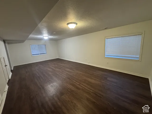 Spacious room featuring wood-finish flooring, neutral-toned walls, and recessed windows with blinds