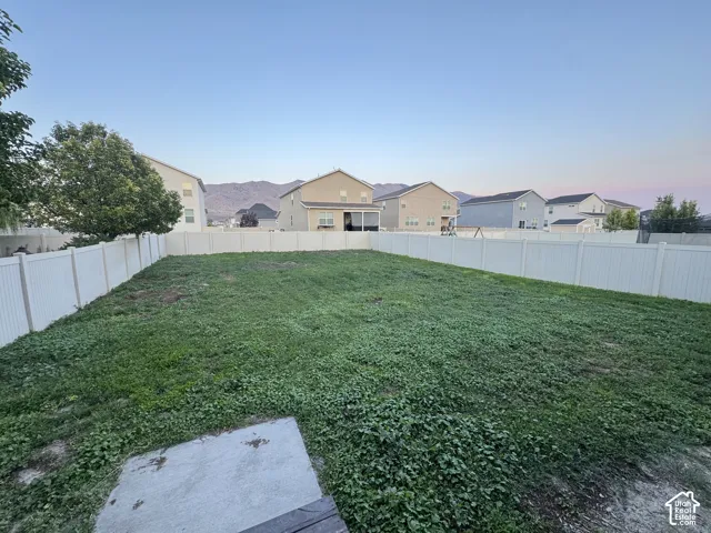 Expansive backyard featuring a large grassy area, privacy fencing, a concrete pad, and distant mountain scenery