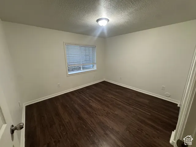 Spacious room featuring dark wood-finish flooring, light-colored walls, a single window with blinds, and a ceiling-mounted light fixture