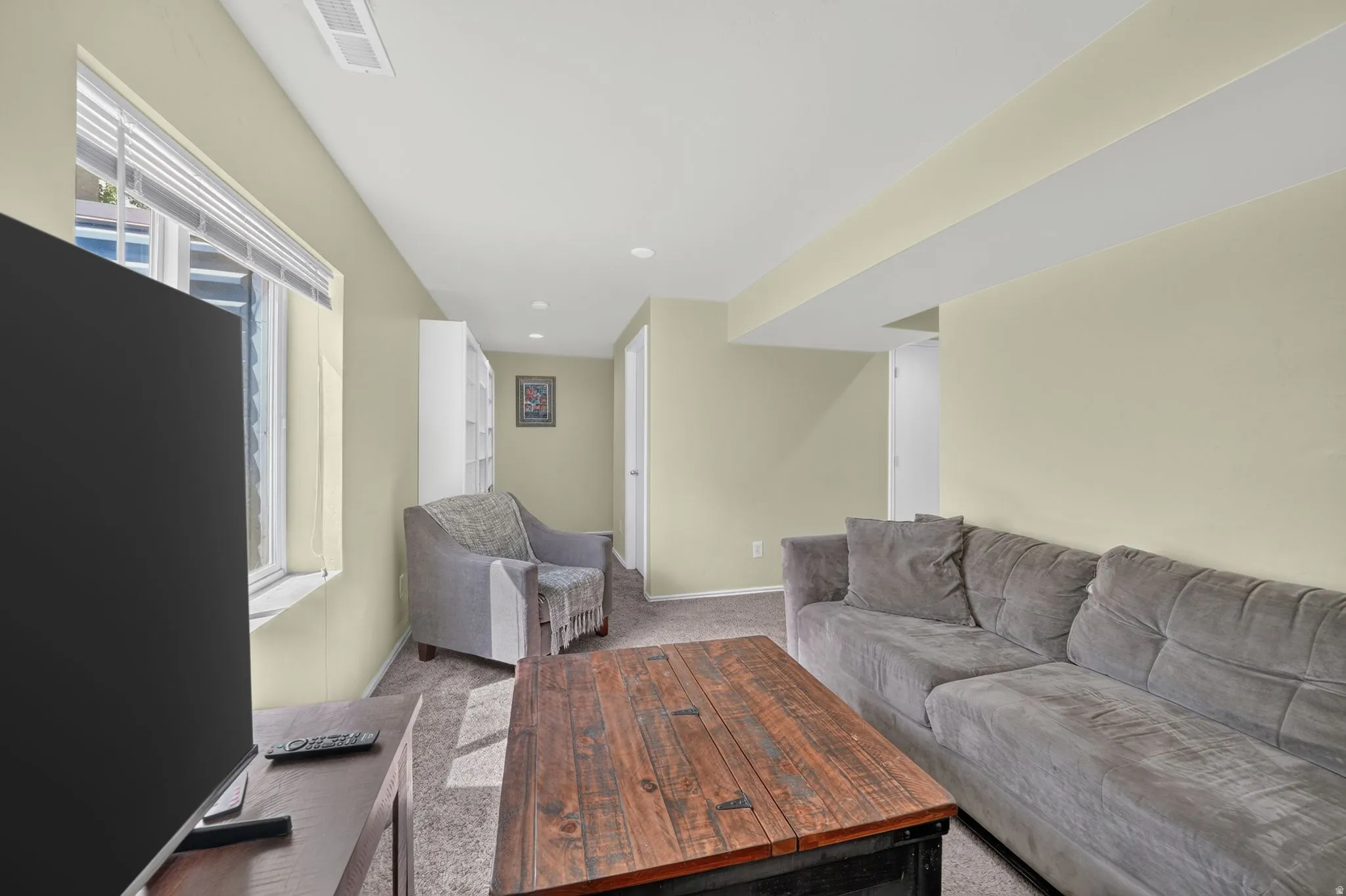 Carpeted living space with recessed lighting, a window featuring blinds, and a built-in shelving unit