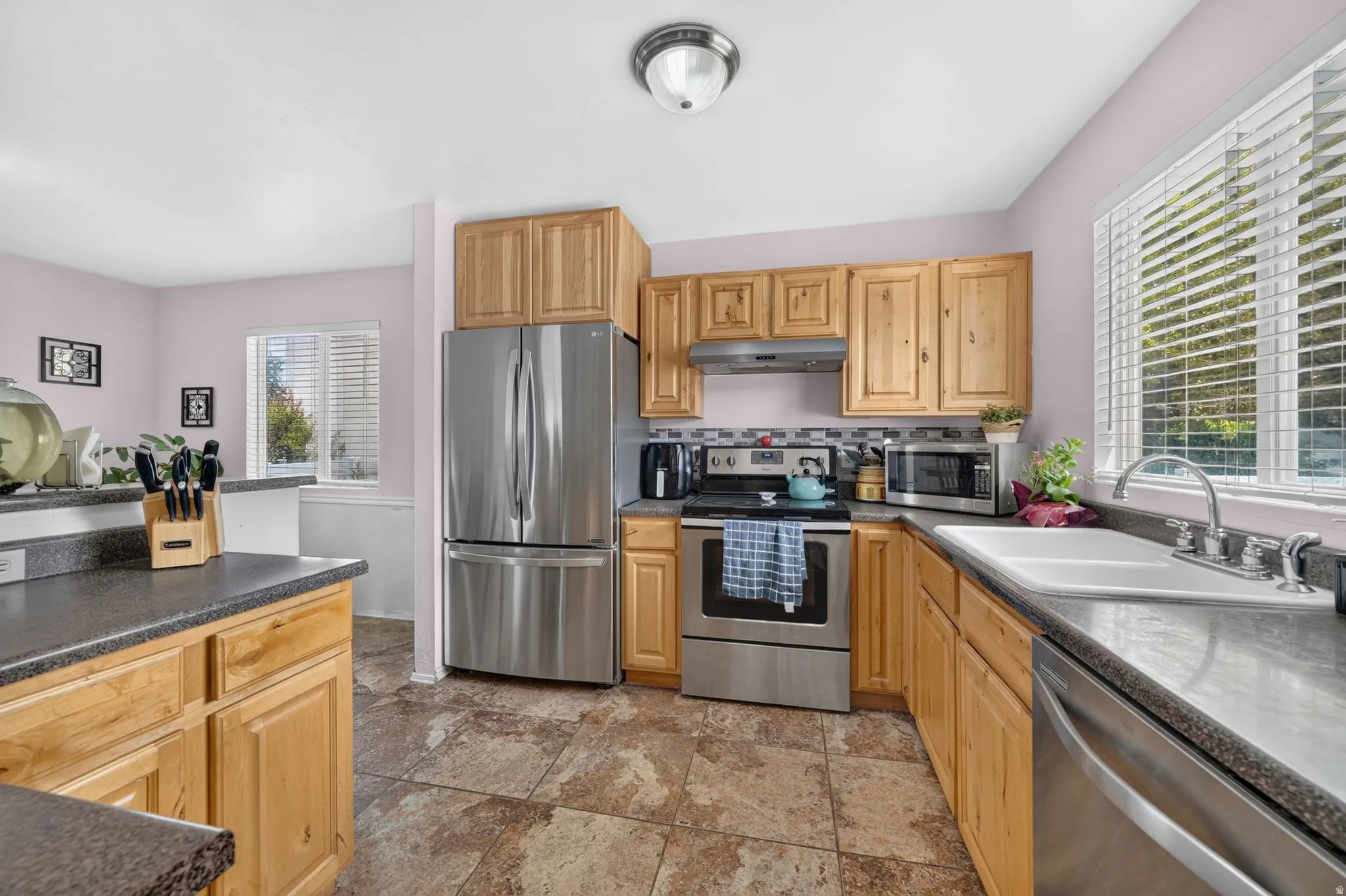 Kitchen featuring wood cabinetry, stainless steel appliances, dark countertops, a tile backsplash, and tile flooring