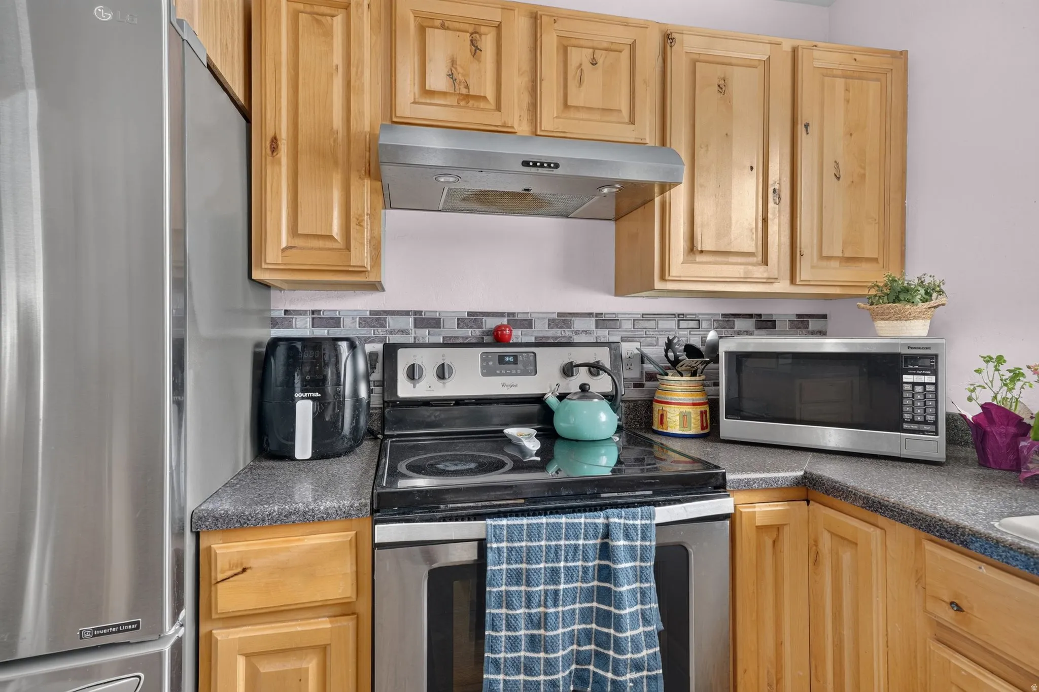 Kitchen featuring light wood cabinetry, dark speckled countertops, and a tiled backsplash