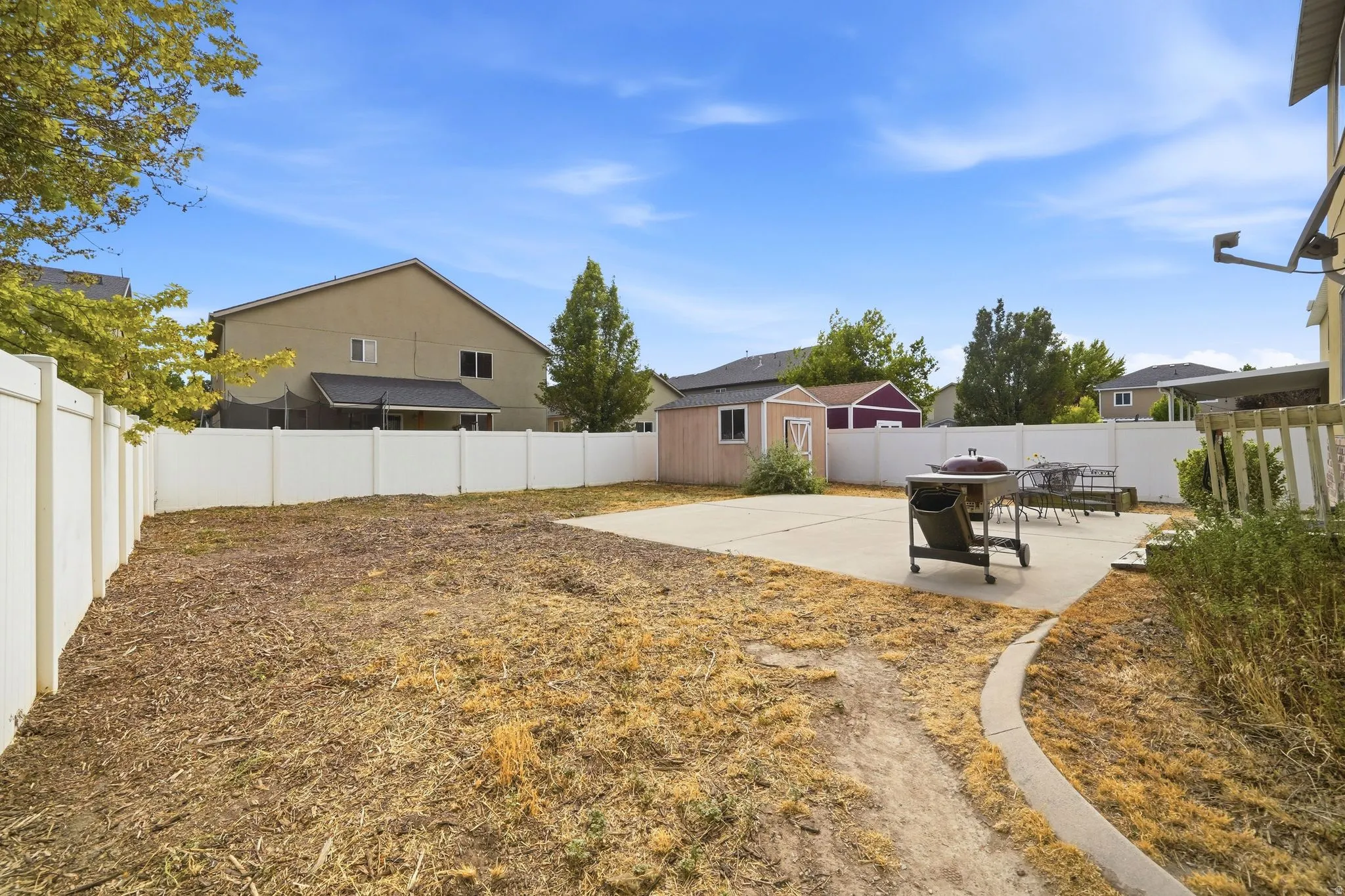 Spacious backyard featuring a large concrete patio, white privacy fencing, and two detached storage sheds