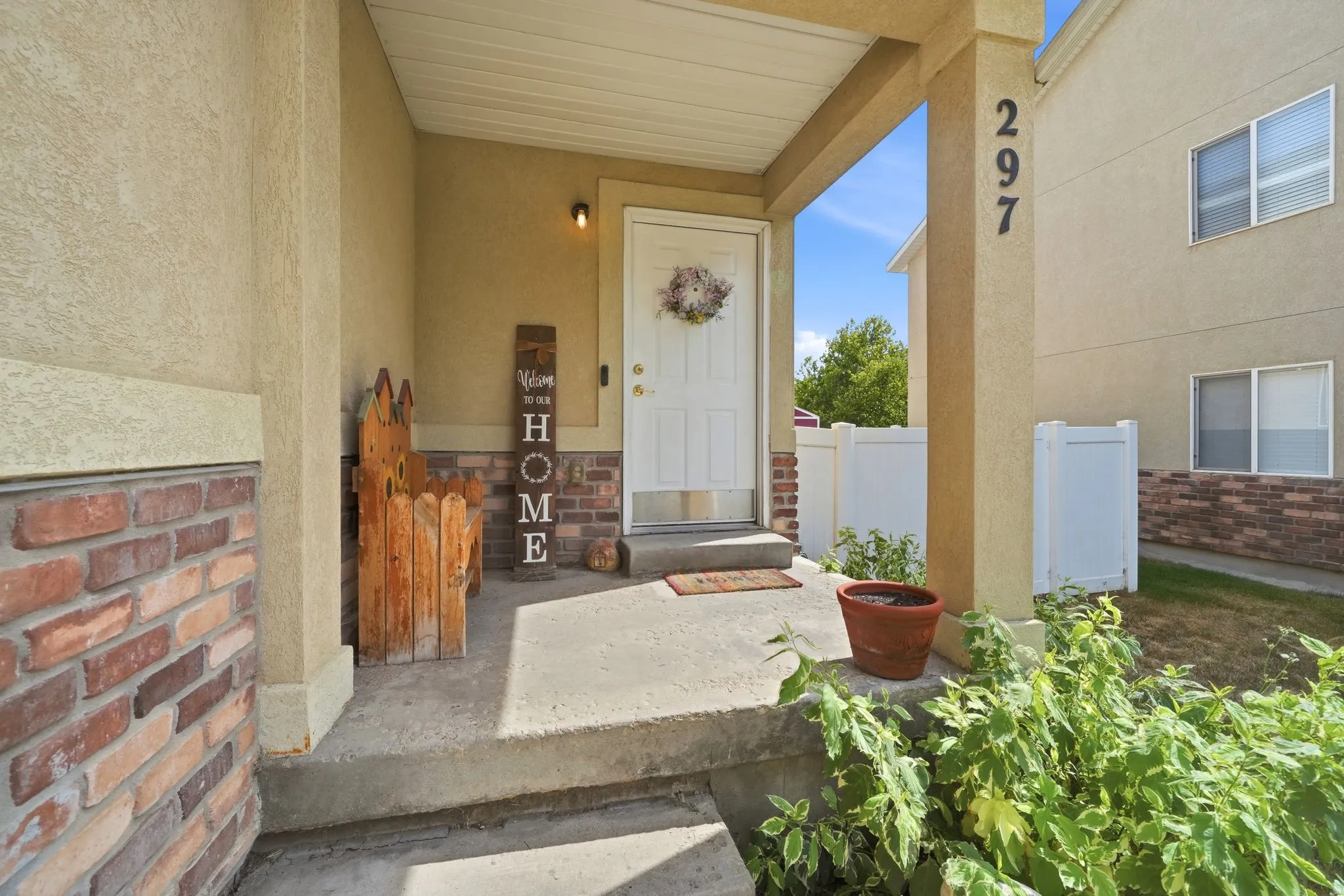 Covered concrete porch entry featuring a white door, brick facade accents, and durable stucco siding