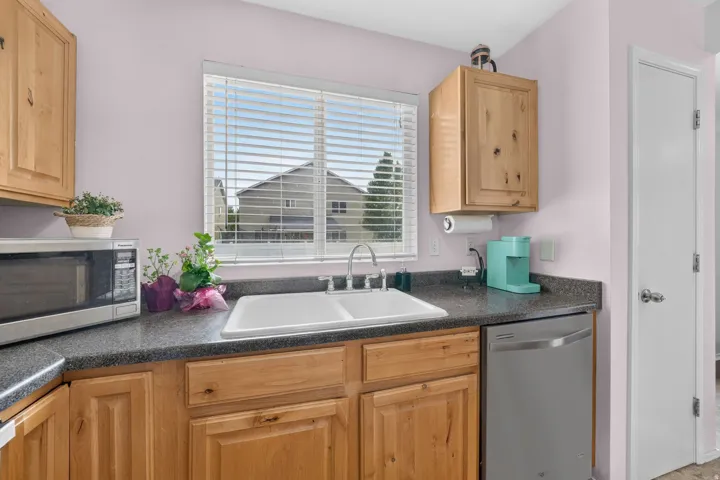 Kitchen featuring a double basin sink, dark speckled countertop, light wood cabinetry, and a stainless steel dishwasher