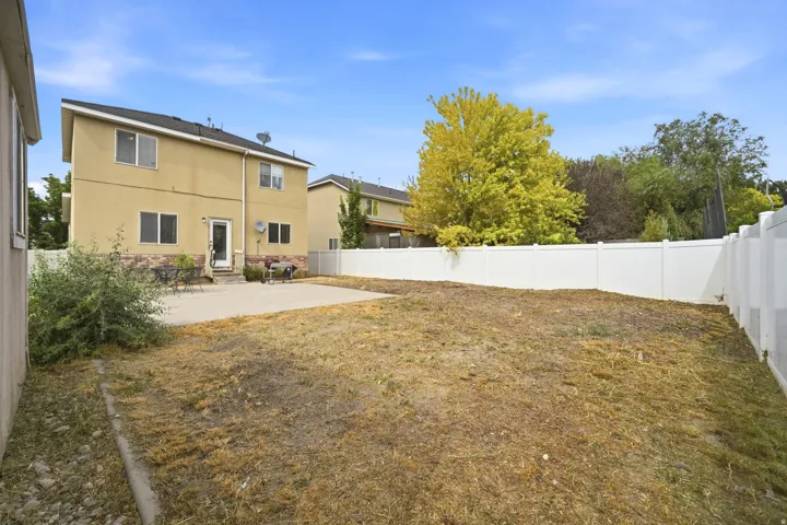 Expansive backyard featuring a concrete patio, a tall privacy fence, and mature trees in the background