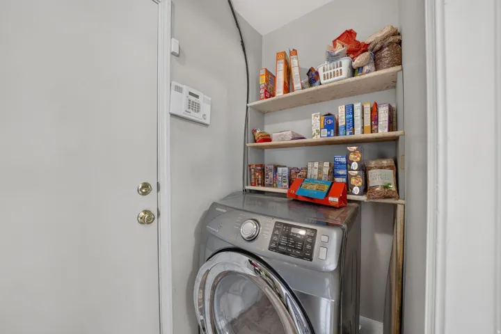 Dedicated laundry area featuring a front-loading washing machine, light-toned walls, and built-in shelving