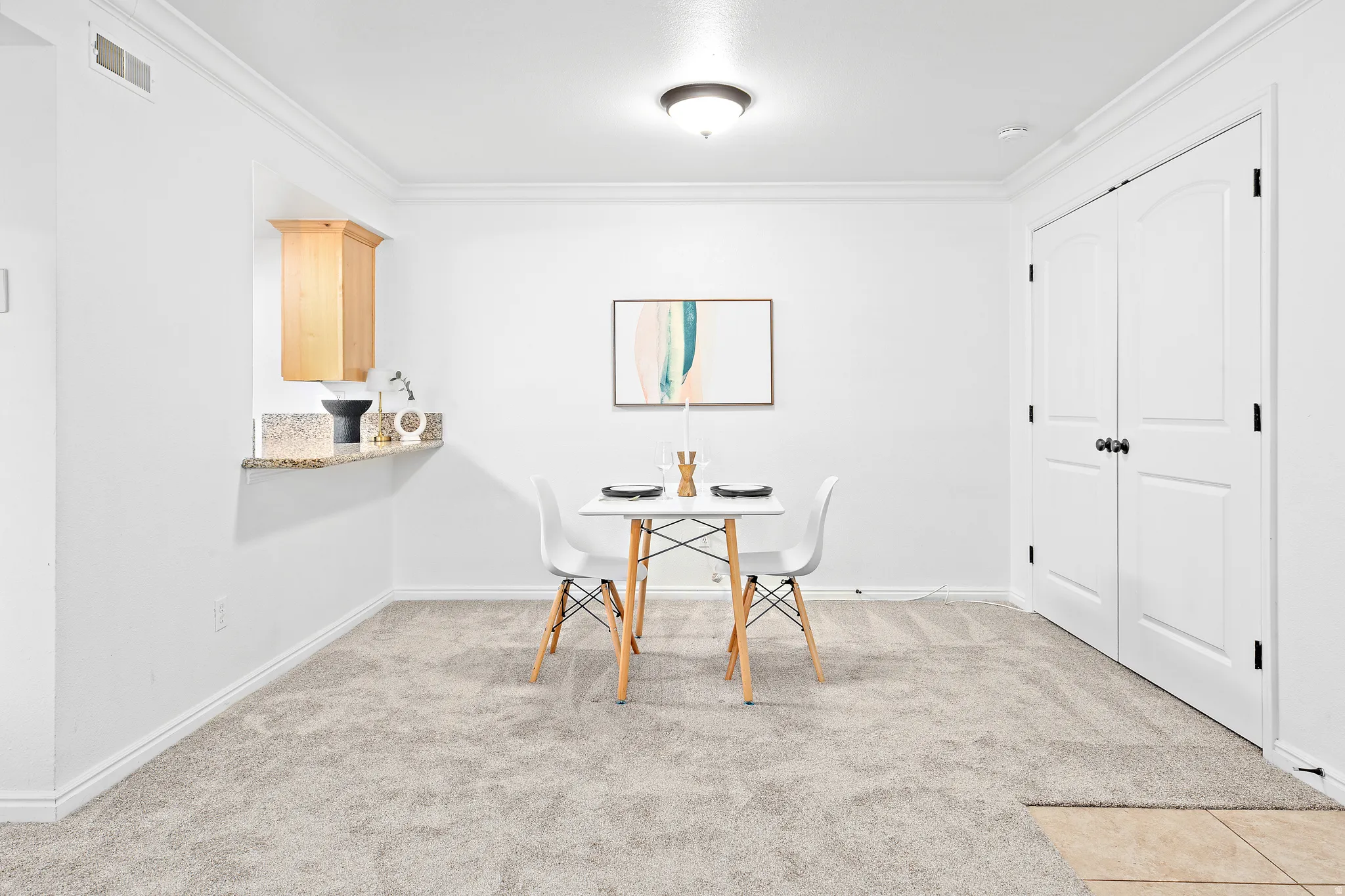 Dining area with light gray carpeting, crown molding, and a built-in granite-top breakfast bar with an overhead wood-finish cabinet