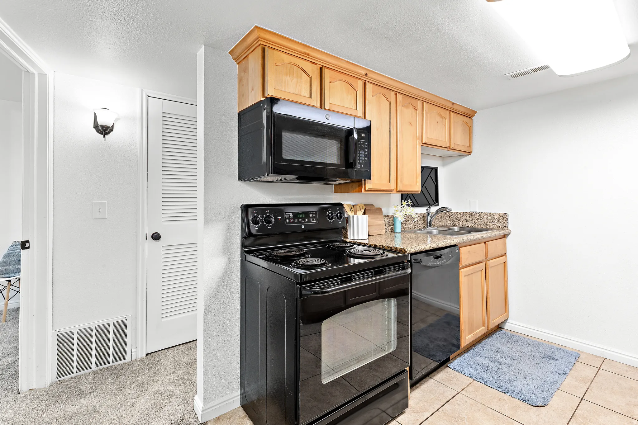 Kitchen featuring wood cabinetry, black appliances including a range and microwave, a dishwasher, and granite-style countertops