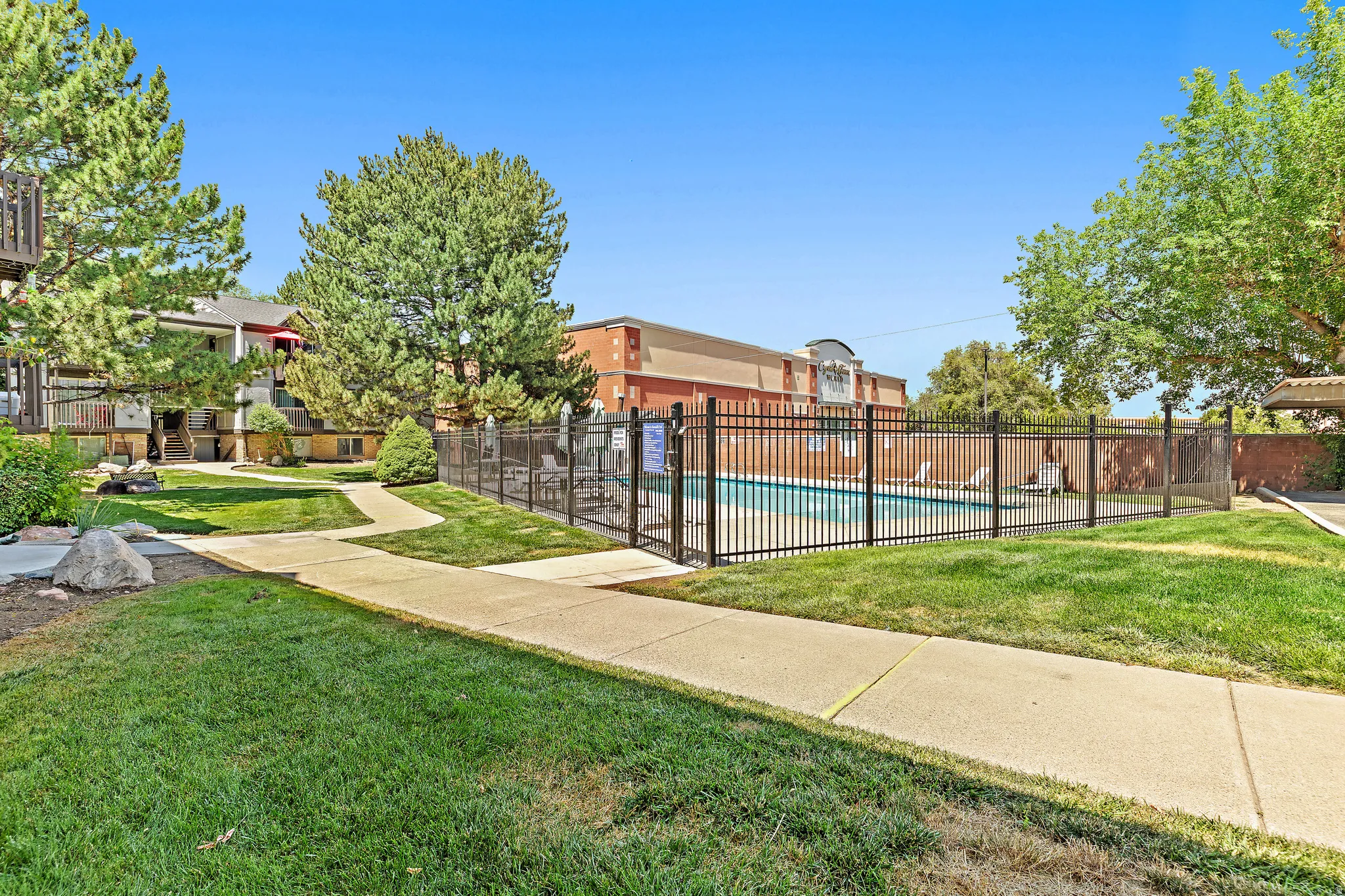 Outdoor swimming pool with black metal fencing, surrounded by a concrete walkway and green lawn