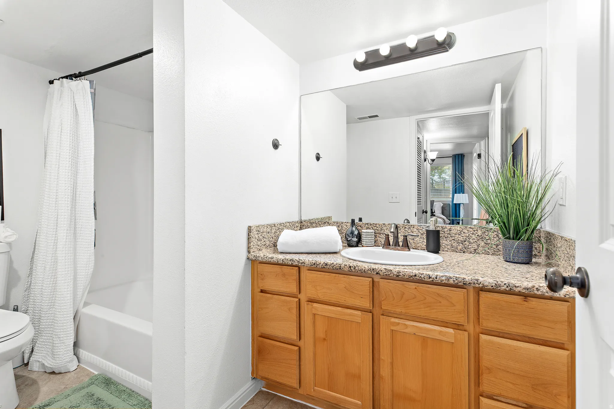 Bathroom featuring a light wood-finish vanity with ample storage, a speckled countertop, and a large wall-mounted mirror