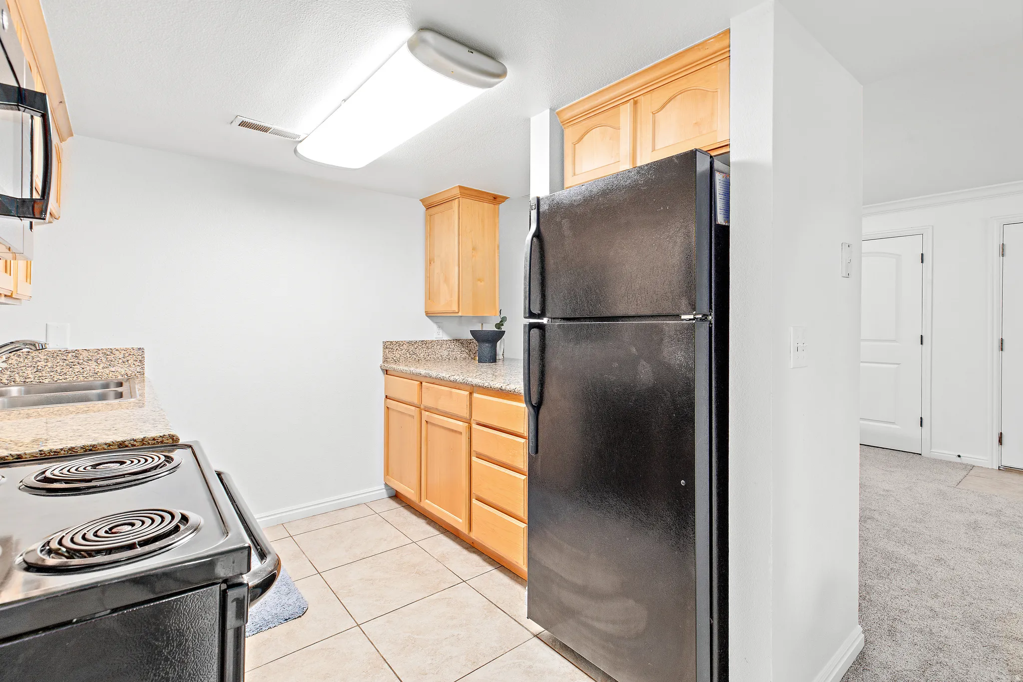 Kitchen featuring light wood cabinetry, stone countertops, integrated sink, and a black electric range