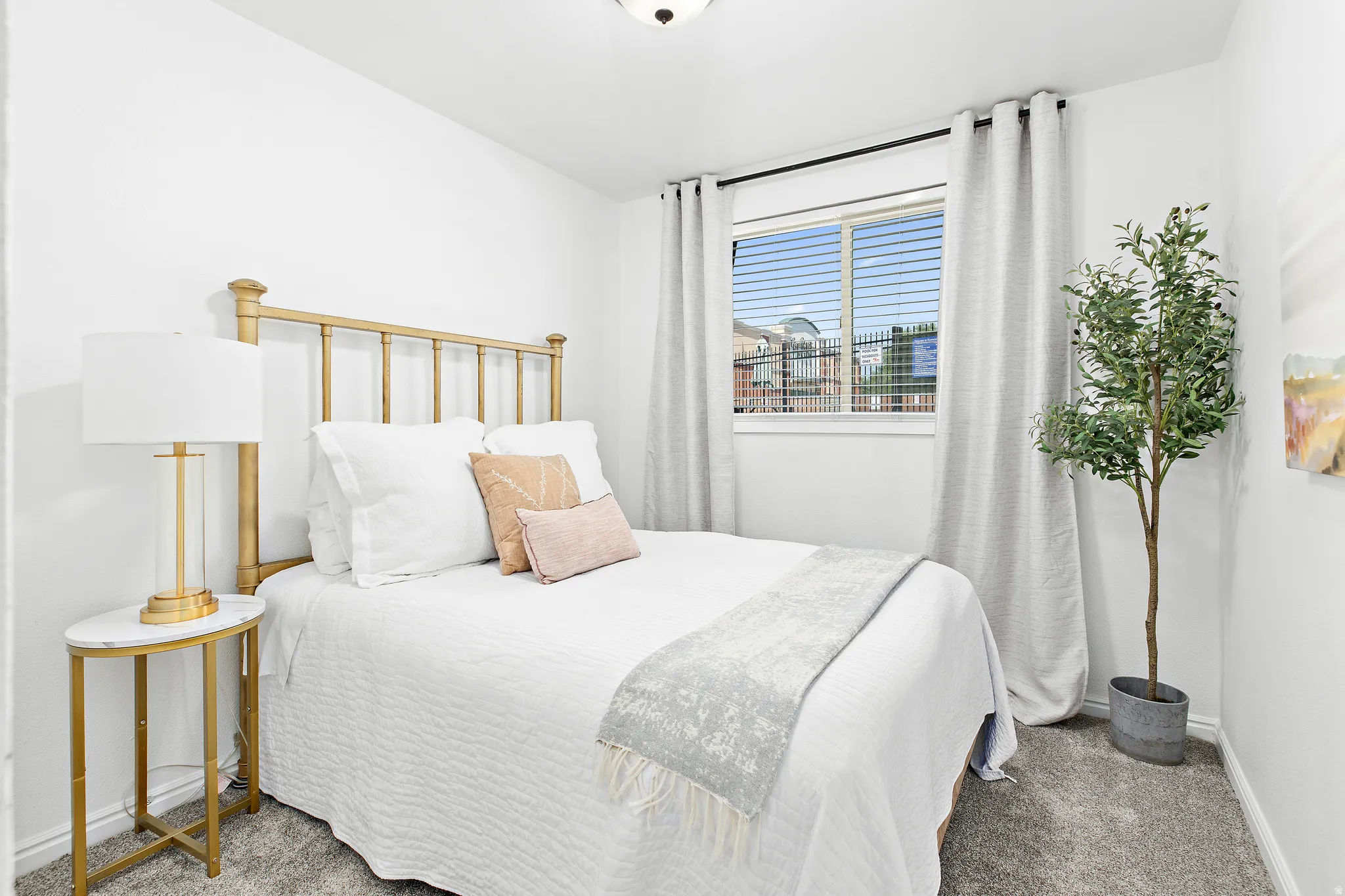 Bedroom with light gray carpeting and a single window featuring horizontal blinds and gray curtains