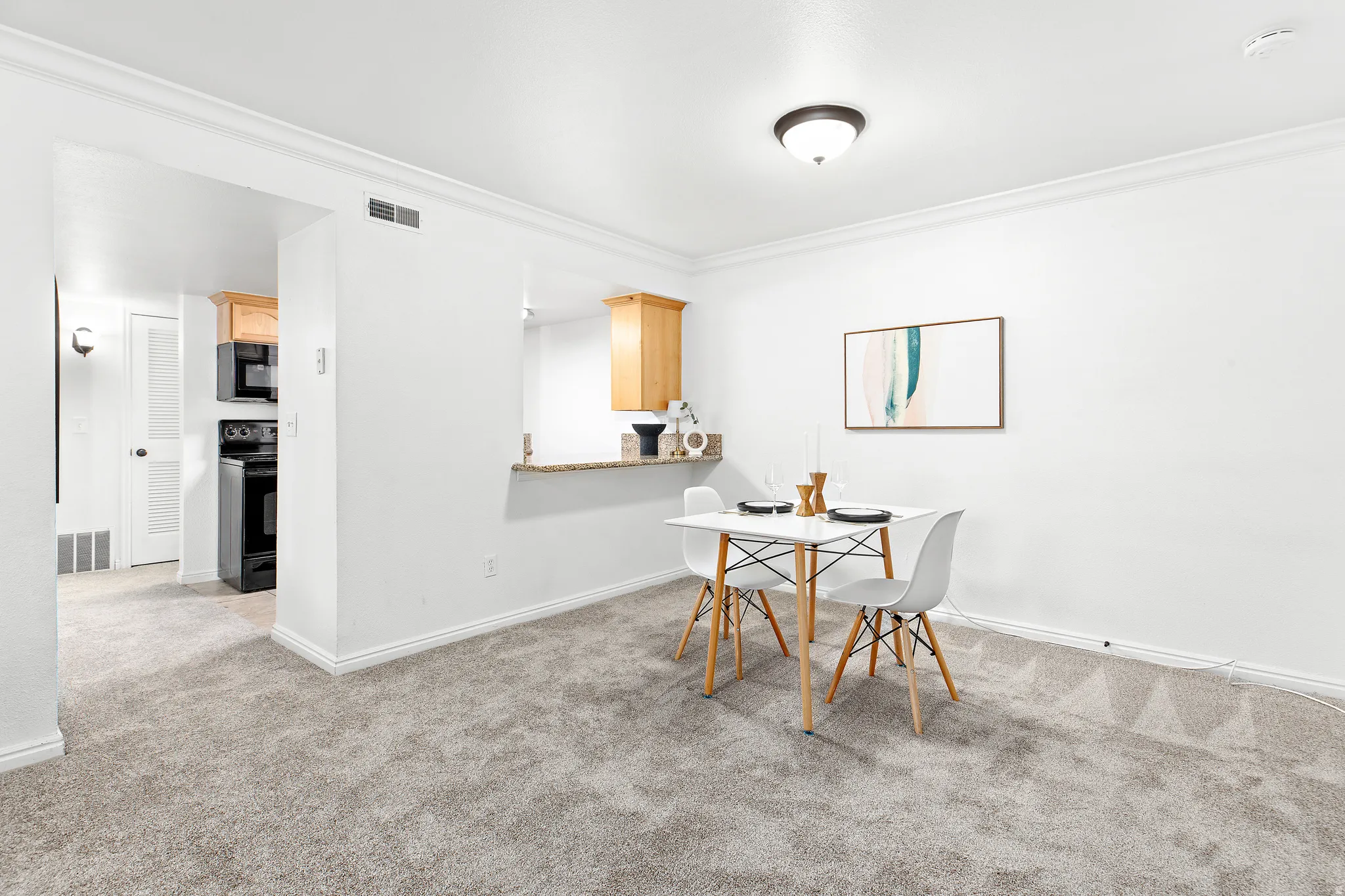 Carpeted living space featuring a breakfast bar with stone-finish countertop, light wood cabinetry, white walls, and crown molding