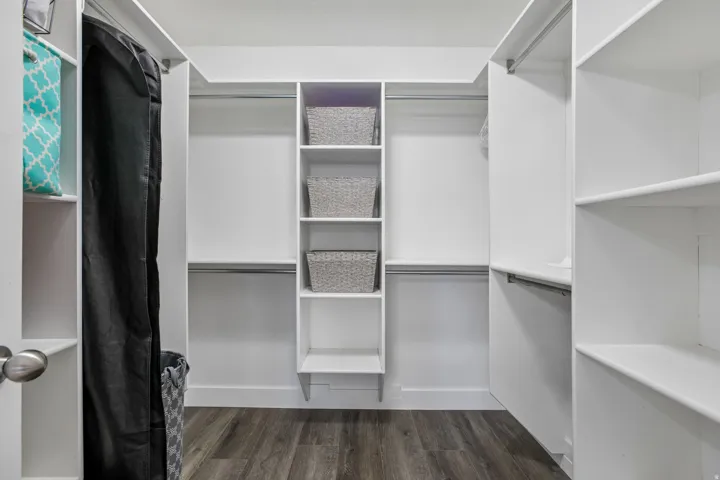 Spacious walk-in closet featuring white built-in shelving, multiple hanging rods, and wood-finish flooring