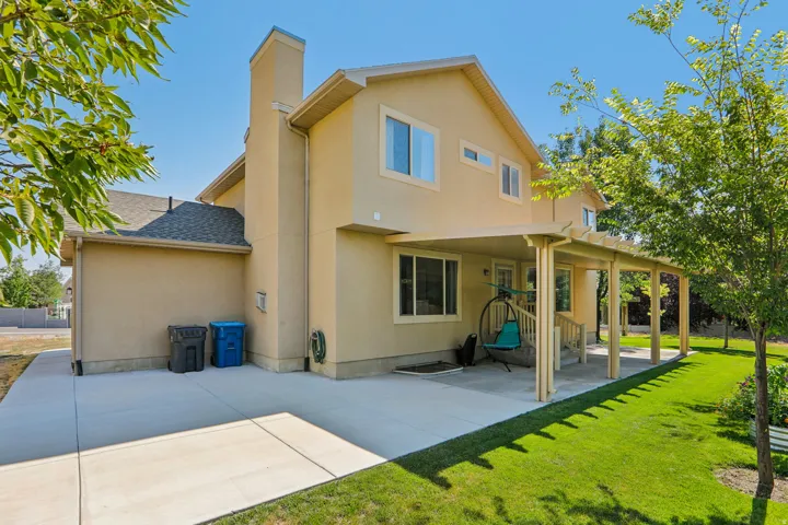 Rear stucco exterior featuring a covered patio, multiple windows, a prominent chimney, and a manicured lawn