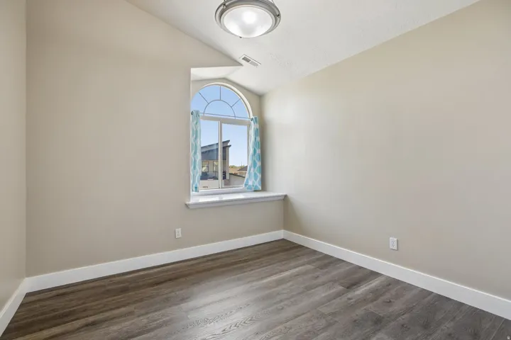 Room featuring an arched window, vaulted ceiling, and wood-finish flooring