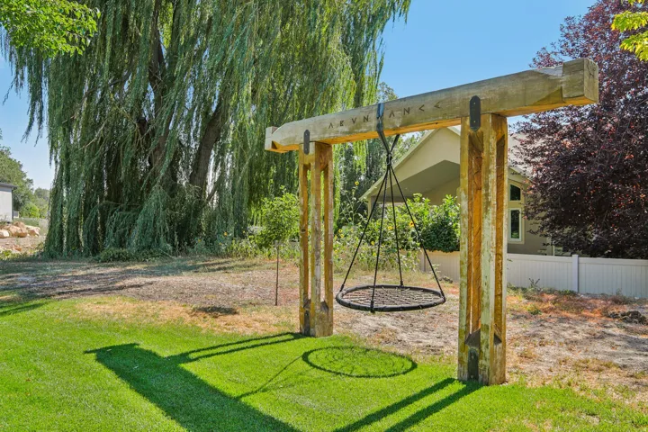 Expansive backyard featuring a custom wooden swing set with a circular swing, manicured lawn, and mature trees including a large weeping willow