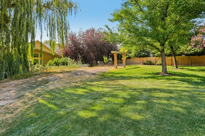 Spacious backyard featuring a manicured lawn, established shade trees, a wooden pergola, and a privacy fence