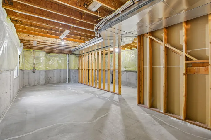 Unfinished basement featuring exposed wood joists, concrete flooring, perimeter insulation, and partial wood framing for future development