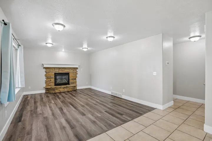 Living area featuring a corner stone fireplace with a white mantel, wood-finish flooring, and multiple flush-mount ceiling lights