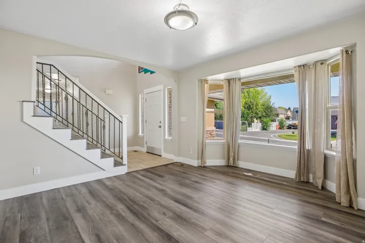 Spacious interior featuring wood-finish flooring, a bay window with natural light, and a staircase with wrought iron balusters
