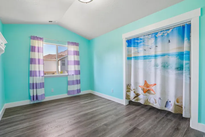 Bright room featuring wood-finish flooring, a vaulted ceiling with a flush-mount light, and a window with white trim