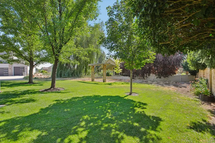 Expansive green lawn featuring mature shade trees, a wooden pergola, and a stone-clad privacy wall