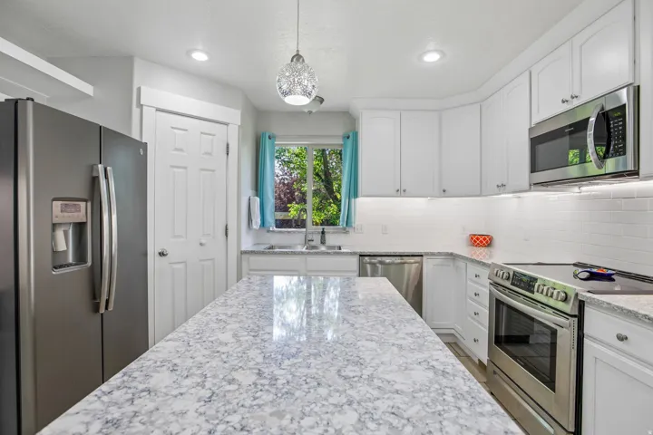 Kitchen featuring a large island with a patterned countertop, white cabinetry, stainless steel appliances, and a subway tile backsplash