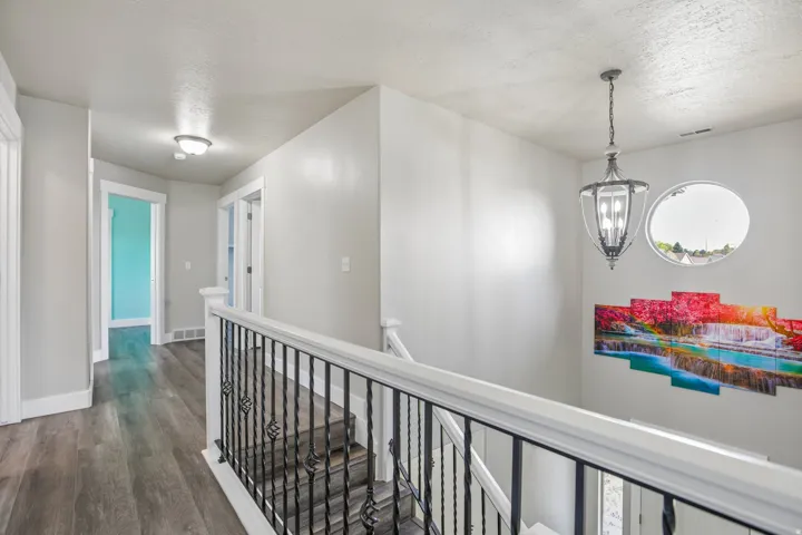 Upper-level hallway featuring wood-finish flooring, white trim, a decorative metal and wood balustrade, and an oval window with an overhead hanging light fixture