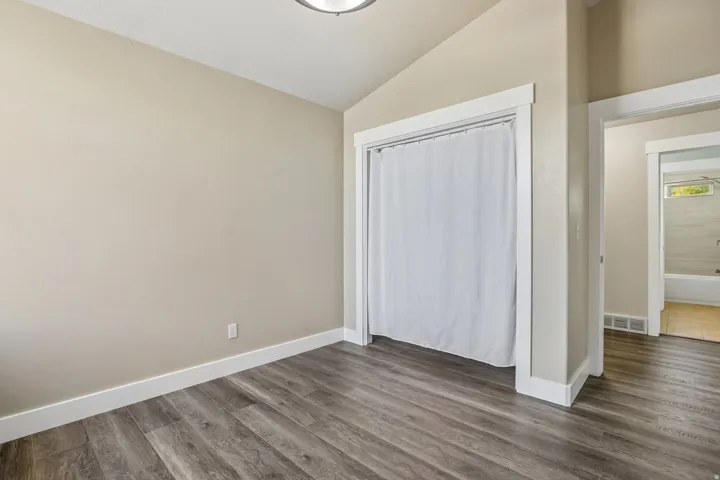 Neutral-toned room featuring wood-finish flooring, white trim, and a built-in closet with a curtain