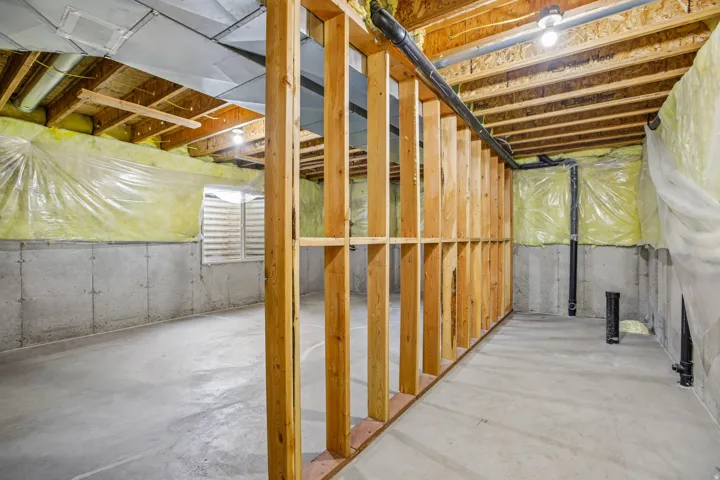 Unfinished lower level featuring concrete flooring, exposed wood framing, and visible utility lines
