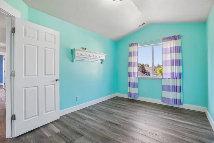 Room featuring vaulted ceiling, wood-finish flooring, and a multi-pane window